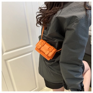 Detail shot of bright orange mini crossbody bag with double buckle straps on a model