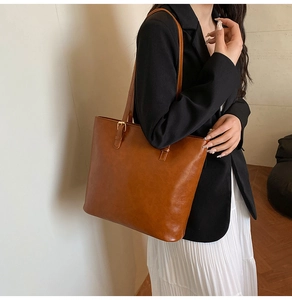 Detail view of large brown faux leather tote bag with thin shoulder straps and gold buckles