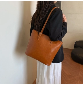 Detail of a brown leather tote bag with thin shoulder straps and gold metal buckle accents