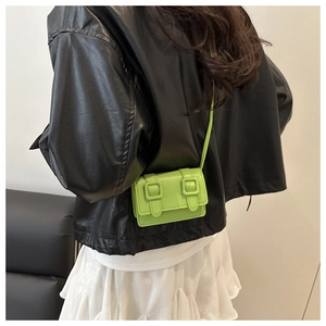 Close-up of a neon green mini crossbody bag with double buckle design on a model