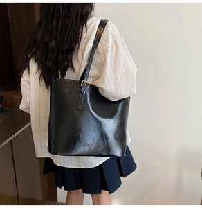 Detail of a black glossy leather tote bag with metal buckle strap worn over the shoulder