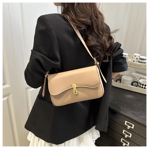 Detailed view of beige leather shoulder bag with gold clasp on a person in a modern interior