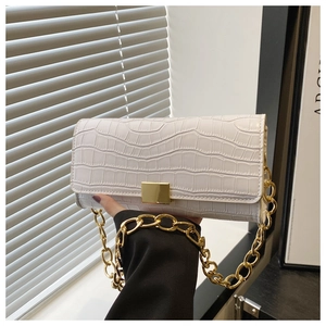 Detail van witte baguette tas met krokodillenpatroon en gouden schakelketting