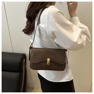 Detail view of brown leather shoulder bag featuring a golden metal lock and minimalist design