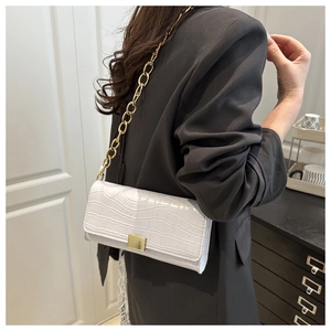 Detail van witte baguette tas met krokodillenpatroon en gouden ketting bij model