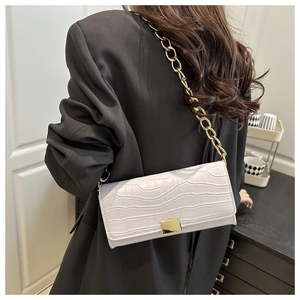 White crocodile pattern shoulder bag with chunky gold chain strap worn on black blazer
