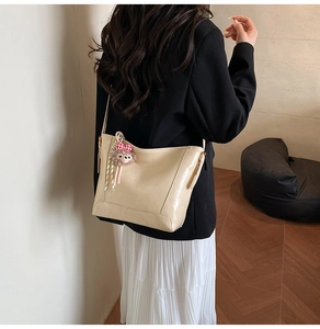 Beige polished leather bucket bag worn by model with cute plush charm and bow