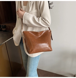 Brown vintage oil wax leather bucket bag worn by model with beige suit and jeans