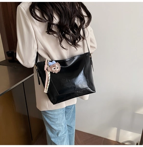 Detail of black glossy hobo bucket bag with pink plush fox pendant and woven strap