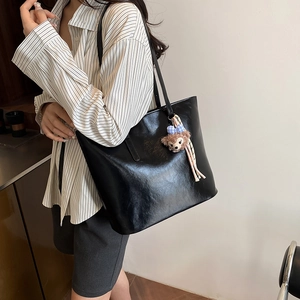 Large black faux leather tote bag with cute plush pendant shown on a striped shirt model