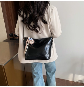Rear view of black glossy faux leather tote bag with plush charm on a model