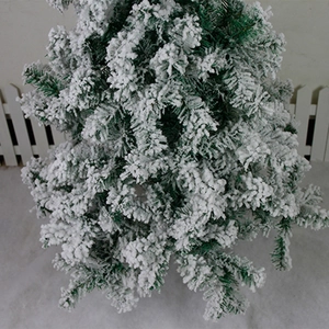 Close-up of artificial flocked Christmas tree branch with thick snow coating and fence
