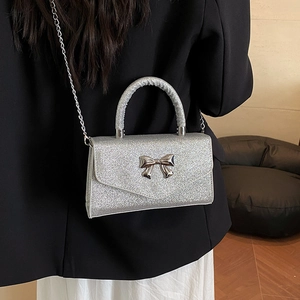 Sac bandoulière pailleté argenté avec nœud papillon en métal porté par un mannequin