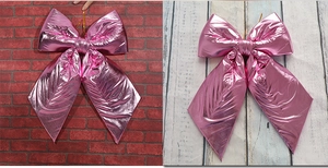 Detail of a large metallic pink decorative bow hanging on a red brick and wood wall