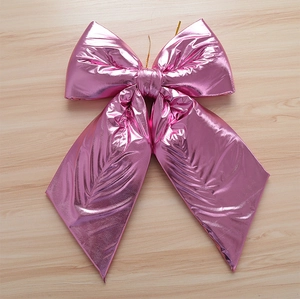 Detail of large metallic pink Christmas bow with a gold wire tie on a light wood surface