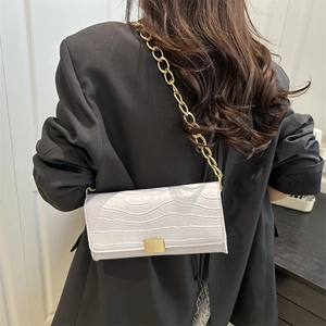 Sac bandoulière blanc motif crocodile avec grosse chaîne dorée porté sur un blazer noir chic