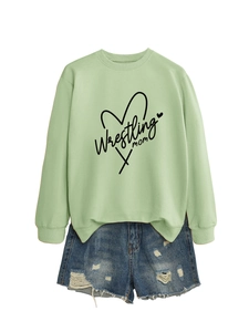 Detail of light green Wrestling Mom sweatshirt with distressed denim shorts on plain background