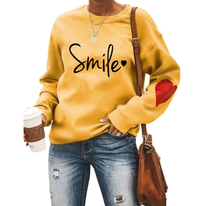 Detail of a yellow sweatshirt featuring a smile print and red heart patch on the sleeve