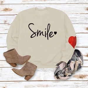 Detail view of cream sweatshirt with black Smile text and red heart patch on sleeve