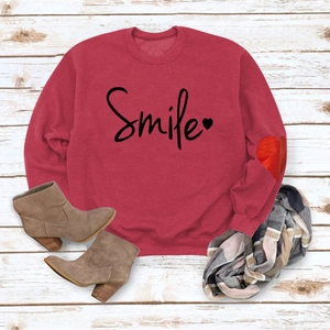 Detail of red crewneck sweatshirt featuring Smile script and heart embroidery on the sleeve