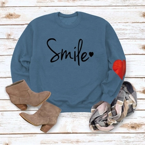Detail of blue crewneck sweatshirt featuring Smile text and red heart print on cuff