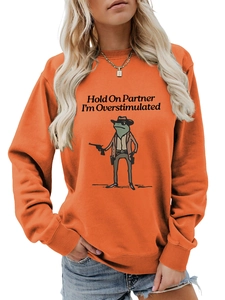 Detail of the cowboy frog graphic and text on an orange crewneck sweatshirt