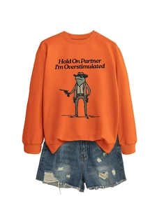Detail of orange sweatshirt with cowboy frog print and distressed denim shorts outfit