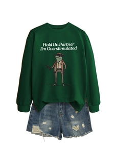 Close-up of green crewneck sweatshirt with cowboy frog print and ripped denim shorts