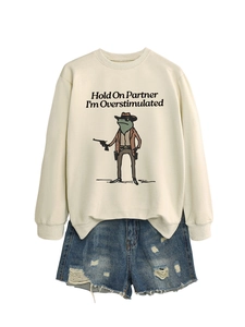 Flat lay of beige oversized sweatshirt with funny cowboy frog graphic and denim shorts