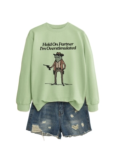 Flat lay of sage green sweatshirt with cowboy frog print and distressed denim shorts