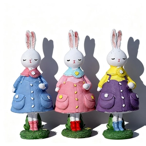 Détail de trois lapins de Pâques en résine avec robes colorées sur socle d'herbe