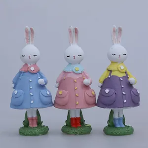 Détail de trois lapins de Pâques en résine avec robes colorées et bottes sur herbe