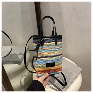 Detail of colorful striped woven crossbody bag with black leather handle and fashion patch