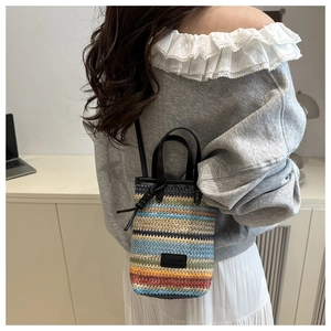 Detail of colorful striped straw woven bucket bag featuring black leather straps and fashion label
