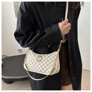 Détail d'un sac croissant beige avec imprimé monogramme et logo métallique sur manteau noir