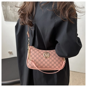 Détail du sac à bandoulière rose nude avec motif M et chaîne dorée porté par un mannequin