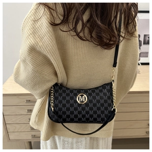Détail du sac sous le bras noir avec motif M et boucle métallique dorée chic