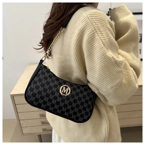 Detail of black leather shoulder bag with gold M logo and chain strap on cream sweater