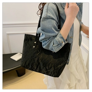 Dettaglio di borsa tote nera con trama stropicciata e borchie con outfit in denim