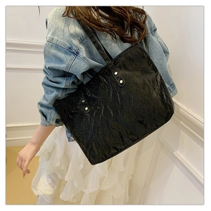 Detail of black textured tote bag with silver rivets worn over a white dress