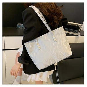 Detail of silver tote bag featuring pleated texture and slim shoulder straps on a model