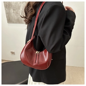 Detail of dark red glossy crescent bag with gold zippers and adjustable shoulder strap