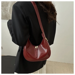 Detailed view of glossy burgundy leather underarm bag with gold zipper and minimalist design