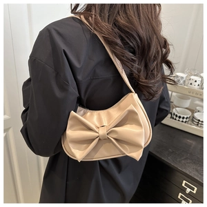 Detail of cream shoulder bag with large bow and leather texture worn by model