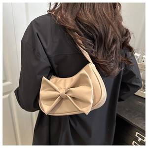 Detail of a beige bow hobo bag with sleek leather texture on a woman's shoulder