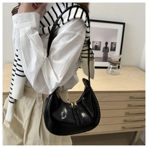 Glossy black crescent shoulder bag with dual zippers shown in a lifestyle setting