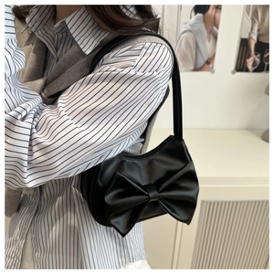 Elegant black shoulder bag with large bow detail shown on a model in a casual outfit