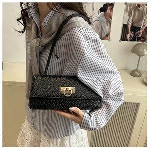 Detail of black woven shoulder bag with vintage gold buckle held by a model