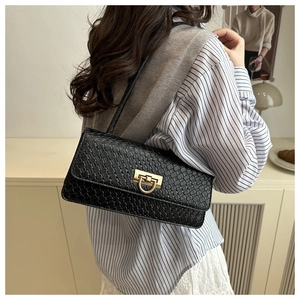 Detail of black baguette bag with woven texture and gold clasp on a model shoulder