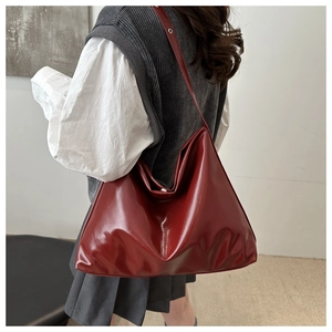 Detail view of burgundy glossy tote bag texture and wide strap on model shoulder